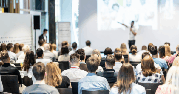Group of people sitting and facing away from the camera. They are all listening to a blurred presenter in the background.