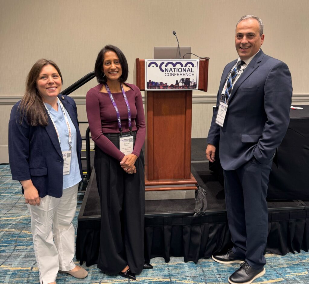 From left to right: Alicia Corey, Chrisna Govin, and Nelson Pedro. All three stand around presentation podium
